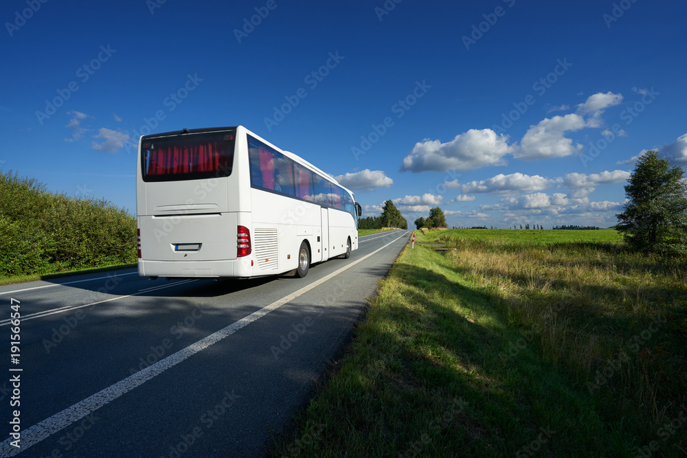 White bus traveling on asphalt road in landscape on a sunny day with blue sky and white clouds