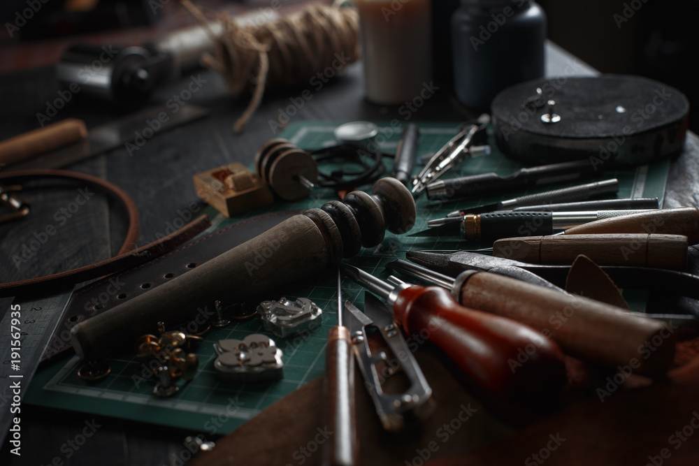 Set of leather craft tools on wooden background. Workplace for shoemaker. Piece of hide and working handmade tools on a work table Set of leather craft tools on wooden background. Workplace for shoemaker. Piece of hide and working handmade tools on a work table