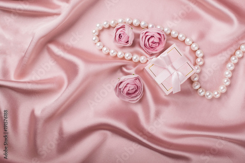 A gift box on a satin background is decorated with flowers and pearls. Copy space. Flat layout.