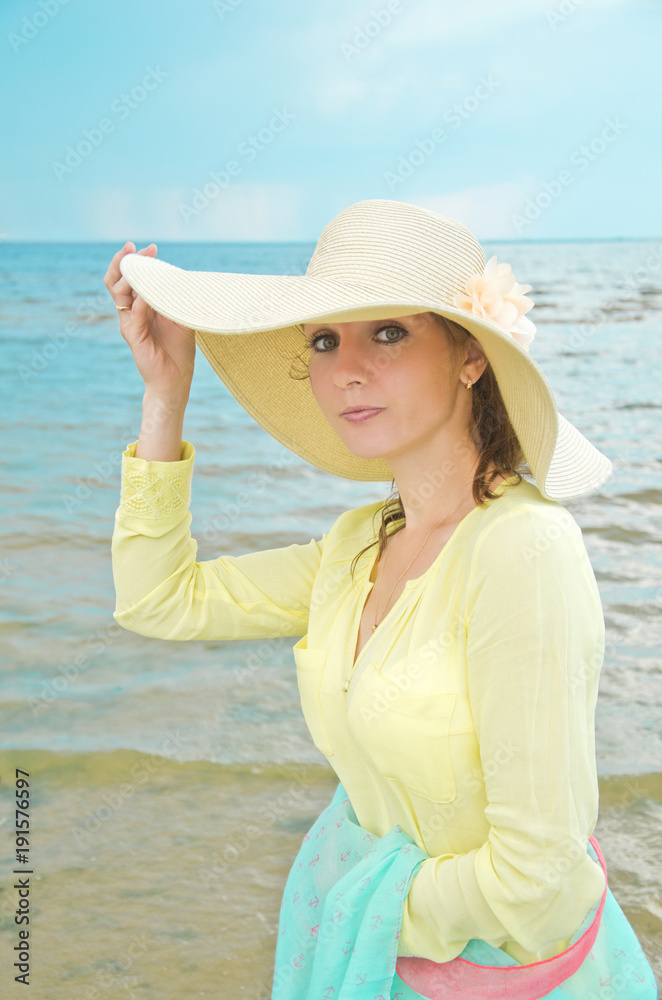 portrait of a young woman in a wide brimmed hat on a warm summer day against a cloudy sky and sea