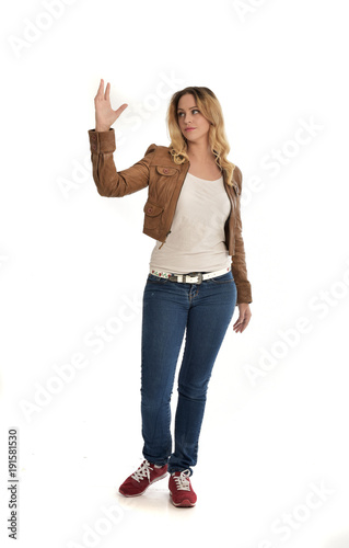 full length portrait of blonde girl wearing simple brown jacket and jeans, standing pose on white studio background.