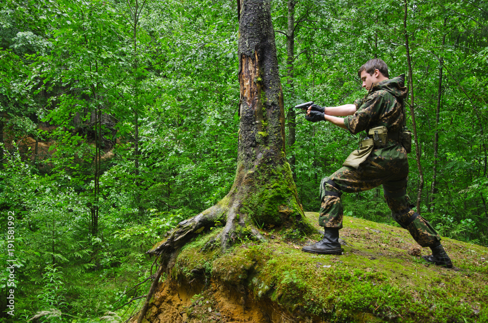 soldier aims and shoots standing in a fighting stand on a hill in the forest