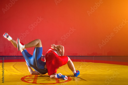 Two strong wrestlers in blue and red wrestling tights are wrestlng and making a suplex wrestling on a yellow wrestling carpet in the gym. Young man doing grapple. photo