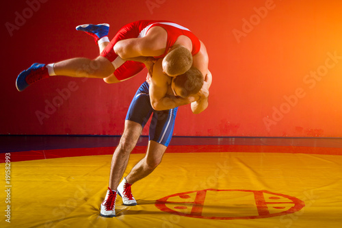 Two greco-roman  wrestlers in red and blue uniform wrestling  on a yellow wrestling carpet in the gym photo