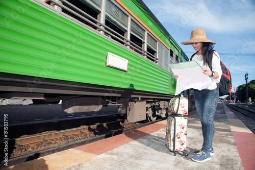 Pretty Asian traveler backpacker female looking map and waiting train at railway station in Thailand.