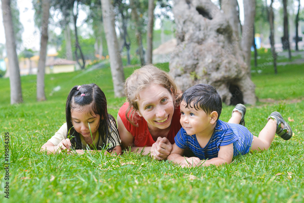 Happy biracial family in the summer park - caucasian mother with her latin children laying on the grass. Happy biracial family in the summer park - caucasian mother with her latin children laying on the grass.