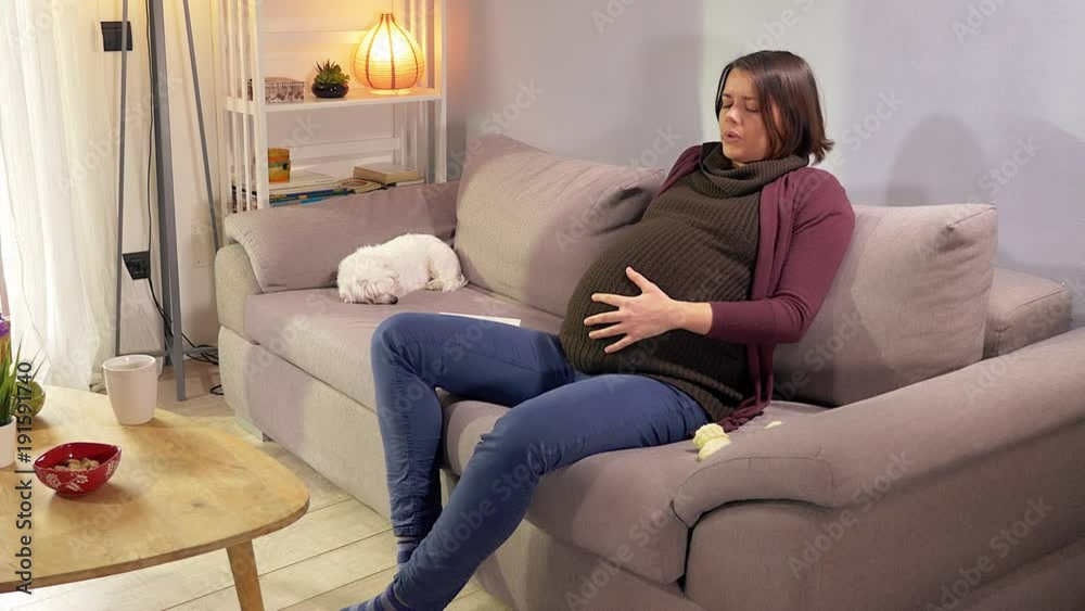 Pregnant woman having contractions at home on sofa calling for help Pregnant woman having contractions at home on sofa calling for help