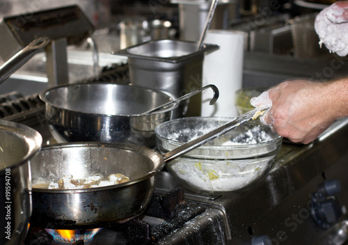 Cooking in a professional restaurant kitchen on the stove with fire in several saucepans