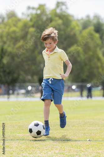 little kid 7 or 8 years old enjoying happy playing football soccer at grass city park field running and kicking the ball excited in childhood sport passion © Wordley Calvo Stock