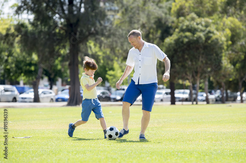 young happy father and excited little 7 or 8 years old son playing together soccer football on city park garden running on grass kicking the ball © Wordley Calvo Stock