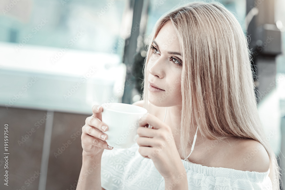 Delicious drink. Attractive blonde young woman holding a cup and drinking coffee while sitting in the cafe Delicious drink. Attractive blonde young woman holding a cup and drinking coffee while sitting in the cafe