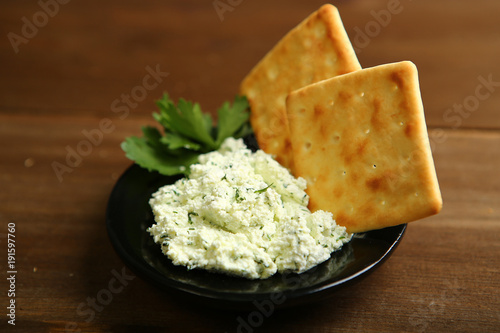 On a dark plate a portion of cottage cheese with greens is decorated with parsley. Low-calorie cookies. Wooden table, dark background. One light source. A healthy diet for those who control their body