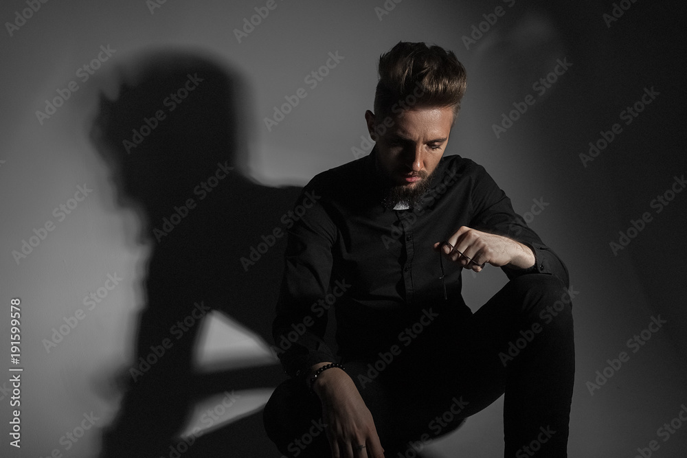 The priest is sitting on the floor with a gloomy shadow from his back against a gray background