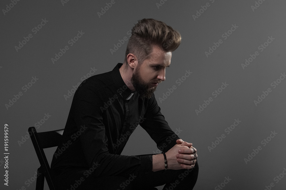 The priest sitting on a chair folded his hands with a cross praying on a gray background The priest sitting on a chair folded his hands with a cross praying on a gray background