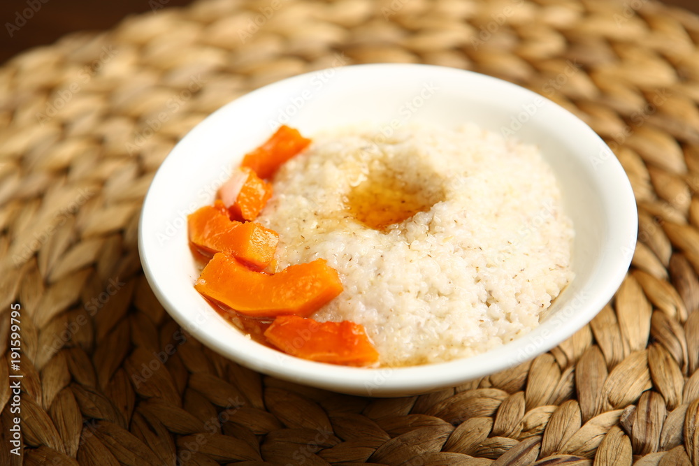 Low-calorie porridge for a healthy diet and lifestyle. Barley with honey and bits of orange pumpkin in a deep white plate. Dark background, wooden table and wicker stand Low-calorie porridge for a healthy diet and lifestyle. Barley with honey and bits of orange pumpkin in a deep white plate. Dark background, wooden table and wicker stand
