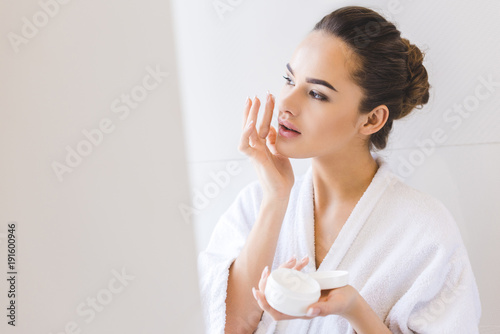 portrait of beautiful woman in bathrobe applying face cream