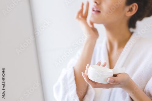 cropped shot of beautiful woman in bathrobe applying face cream photo