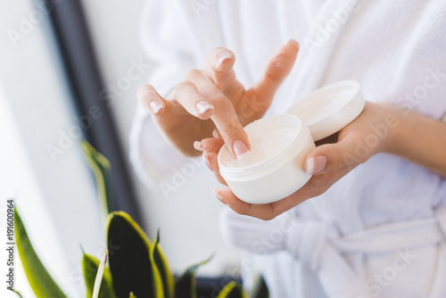 partial view of woman holding face cream in hands