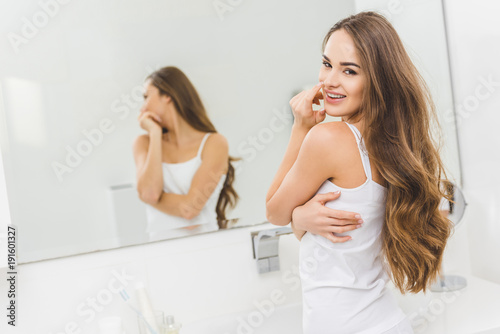 portrait of smiling beautiful young woman looking at camera in bathroom at home