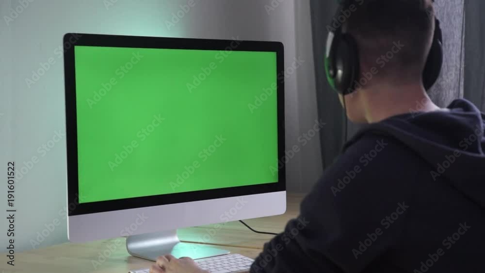 Young man looks at the monitor on the table and play computer games - green screen Young man looks at the monitor on the table and play computer games - green screen