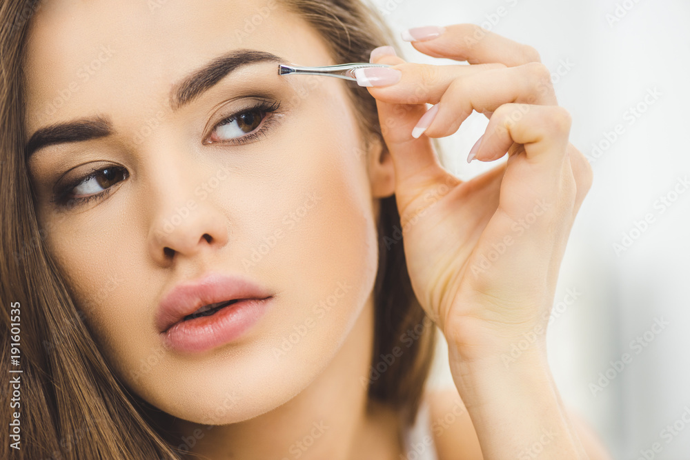 portrait of young woman plucking eyebrows with tweezers portrait of young woman plucking eyebrows with tweezers