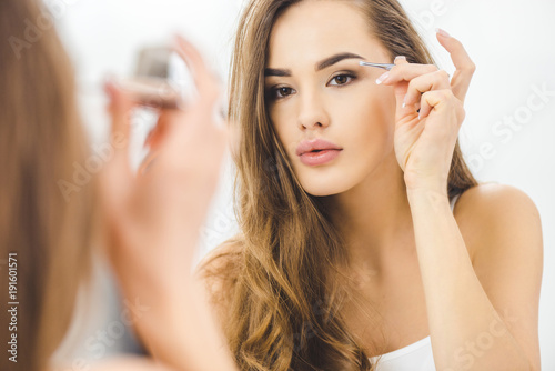 young woman plucking eyebrows with tweezers