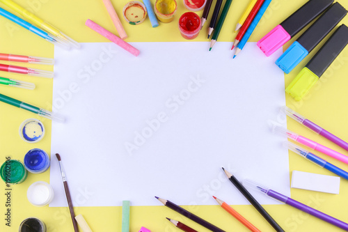 paper with colored crayons, brush, pencils and paints on yellow background. Top view . Flat lay image.Working desk table concept.