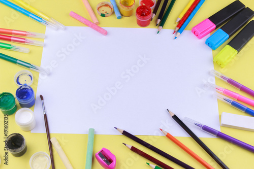 paper with colored crayons, brush, pencils and paints on yellow background. Top view . Flat lay image.Working desk table concept.