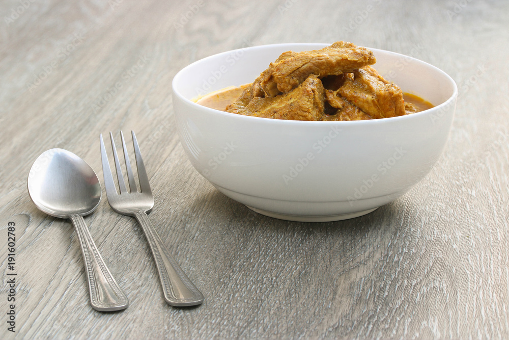 Thai Red curry with pork ribs in white bowl on Galangal leaf and wooden background. , Thai Southern style. Thai Red curry with pork ribs in white bowl on Galangal leaf and wooden background. , Thai Southern style.