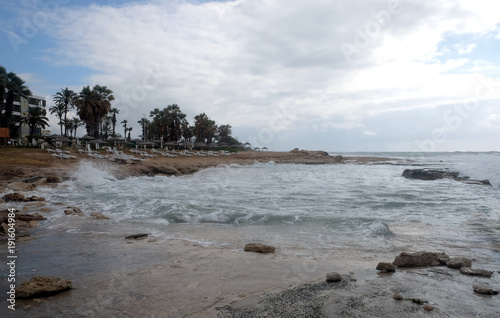 Empty beach on the seaside in resort place with hotel buildings and palm trees in low season in the evening against the backdrop of incoming waves photo