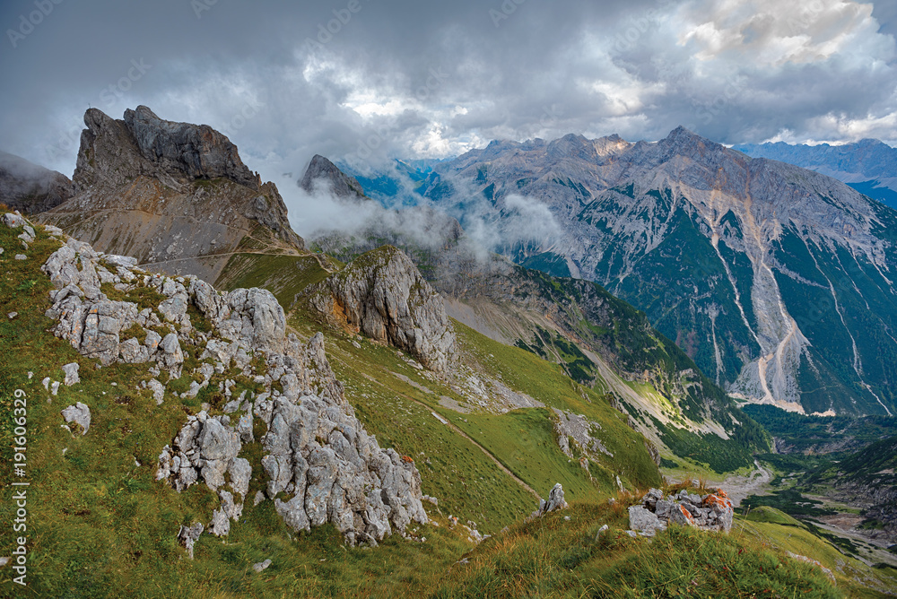 Fototapeta premium Rocks on a mountain grassy slope under dramatic clouds