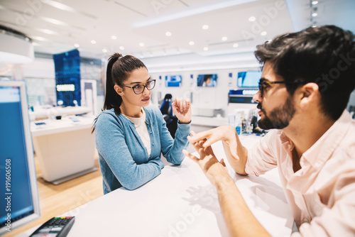 Beautiful young brunette talking with employe in the tech store.