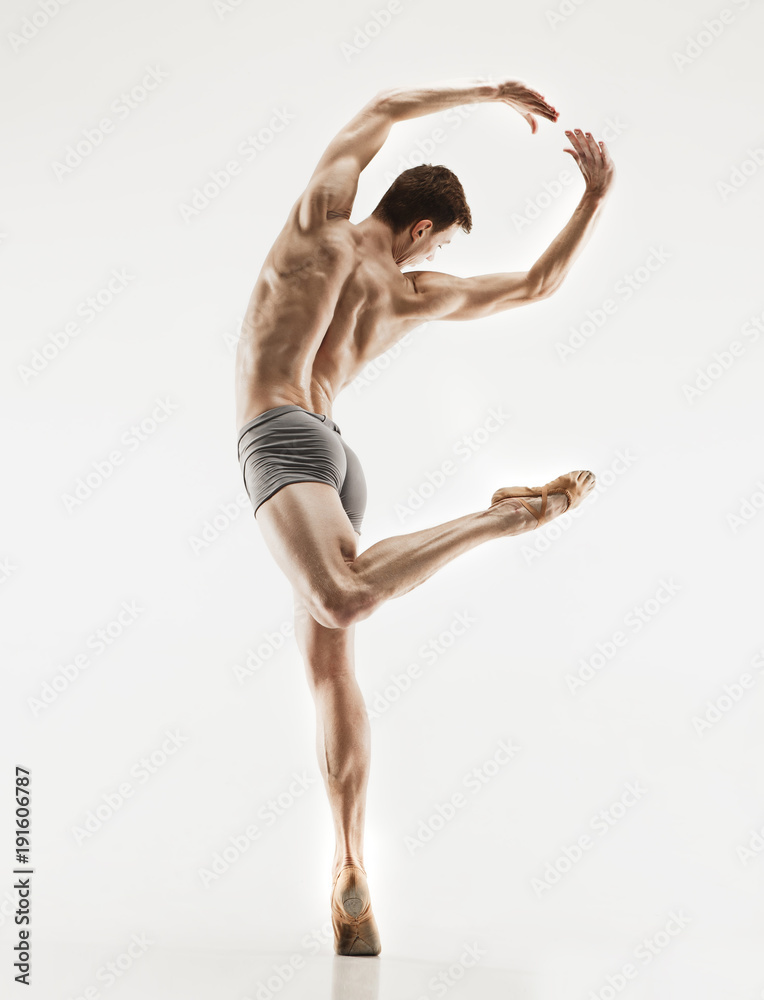 Athletic ballet dancer in a perfect shape performing over the grey background.