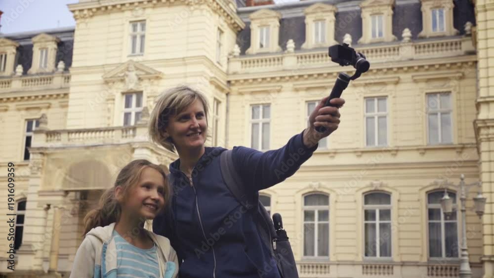 Woman with kid tourists capturing themselves with small personal camera exterior of European castle