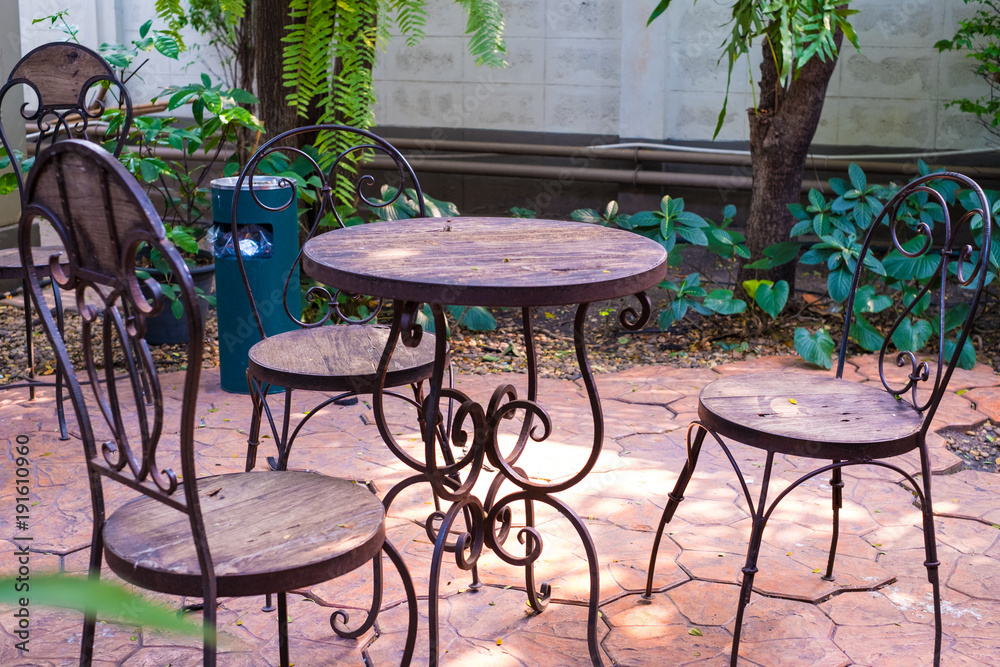 Steel chairs and tables with wooden seat and tree on stone floor in the garden