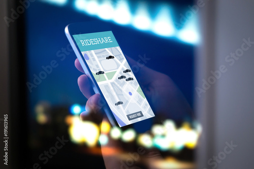 Ride sharing and carpool mobile application. Rideshare taxi app on smartphone screen. Modern online people and commuter transportation service. Man holding phone late at night. City street lights. photo
