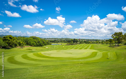 Fototapeta Naklejka Na Ścianę i Meble -  Green grass and trees at golf course with blue cloud sky background 