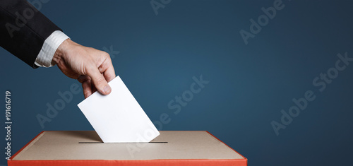 Voter Holds Envelope In Hand Above Vote Ballot On Blue Background. Freedom Democracy Concept photo