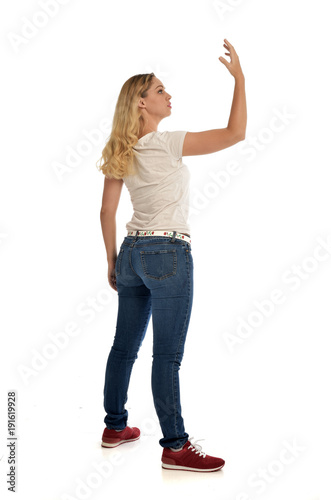 full length portrait of blonde girl wearing simple white shirt and jeans, standing pose, isolated on white studio background.