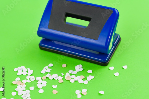 Single blue metal mechanical hole puncher and lot of round white confetti on blank green paper photo