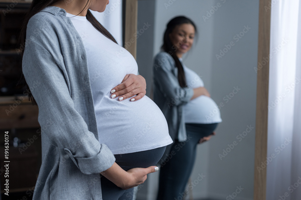 Φωτογραφία african american pregnant woman looking at her belly in mirror