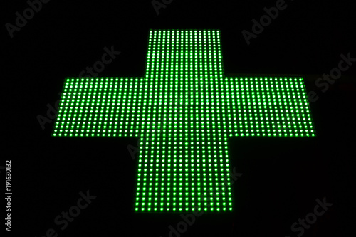 Green LED cross pharmacy and hospital hanging on the street is isolated in black