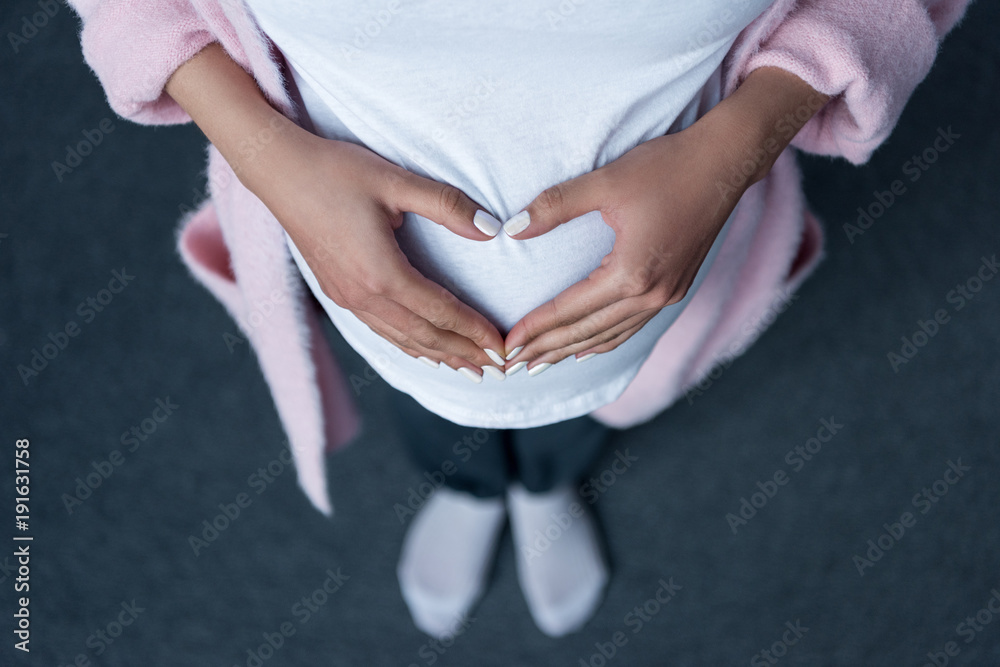 cropped view of pregnant girl making heart symbol with hands on her belly