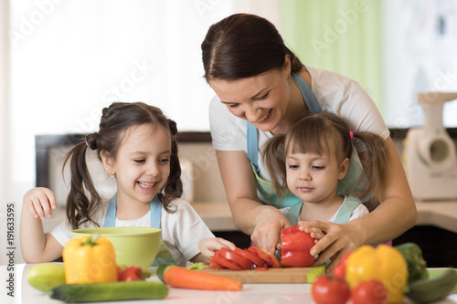 Happy mother and her daughters enjoy making healthy meal together at their home