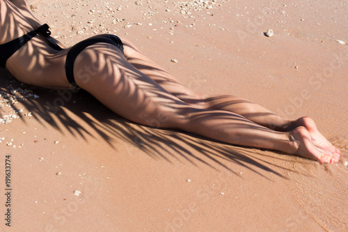 Beautiful luxury slim girl in a black bikini on the beach with palm leaf shadow. Outdoor summer lifestyle image of young pretty woman outfit and sunglasses, fun ,joy, emotions.