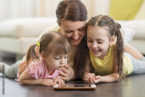 Happy mother and children using digital tablet on floor at home