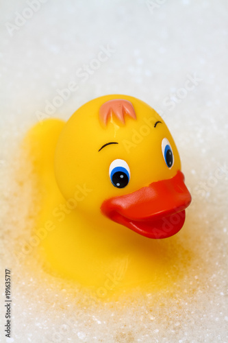 Toy plastic yellow duck floating in a bath surrounded by soap suds