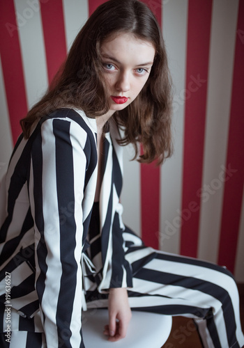 Sexy lady in stylish striped suit posing on red background. Vogue fashion style