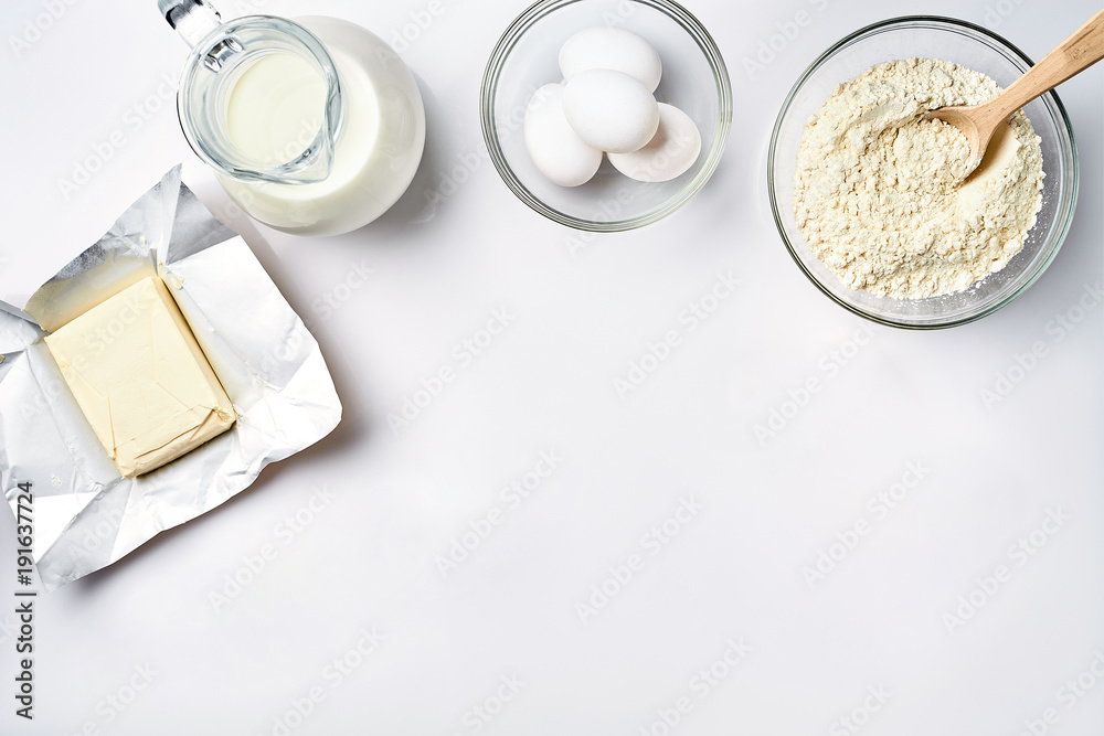 Wheat flour in the glass bowl, cream in a glass jar, butter, chicken eggs - ingredients for the dough, top view Wheat flour in the glass bowl, cream in a glass jar, butter, chicken eggs - ingredients for the dough, top view