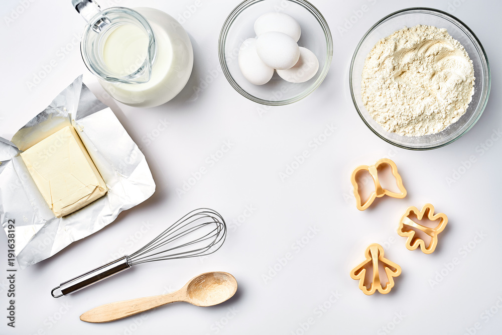 Objects and ingredients for baking, plastic molds for cookies on a white background. Flour, eggs, whisk, milk, butter, cream. Top view, space for text Objects and ingredients for baking, plastic molds for cookies on a white background. Flour, eggs, whisk, milk, butter, cream. Top view, space for text